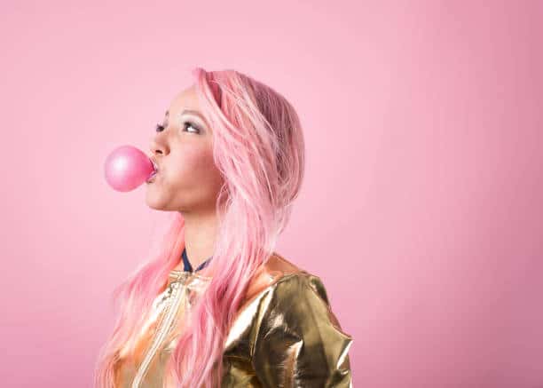Jeune fille aux cheveux rose qui fait une bulle de chewing gum